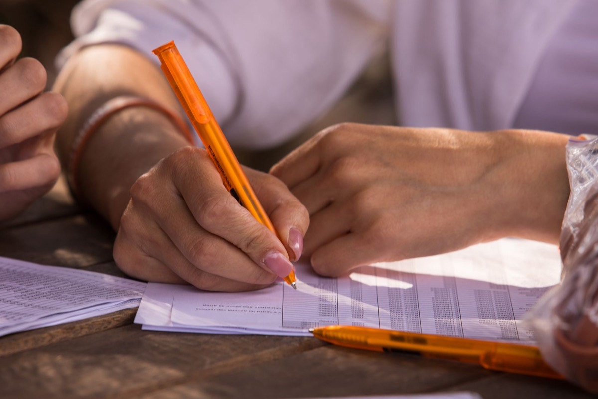 Hands writing with an orange pen on printed forms at a desk