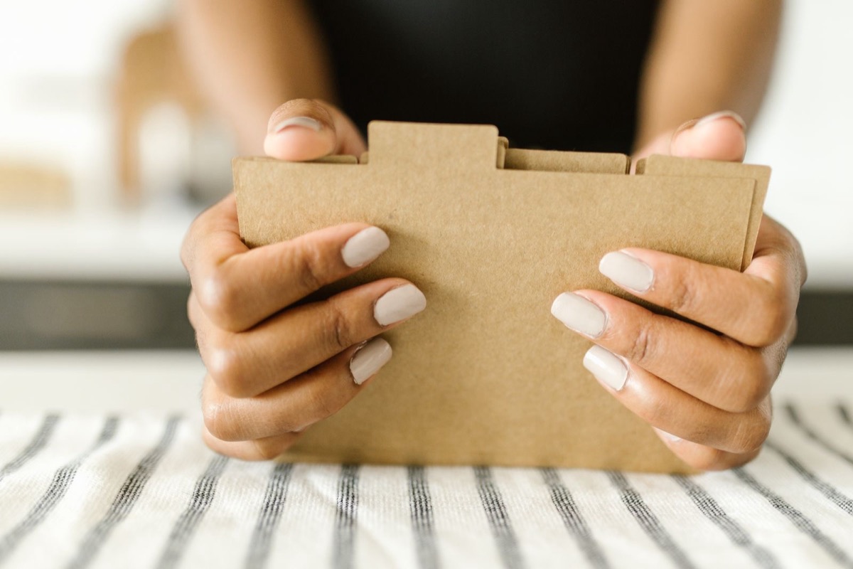 Two hands holding a closed kraft cardboard folder with an index tab above a striped cloth