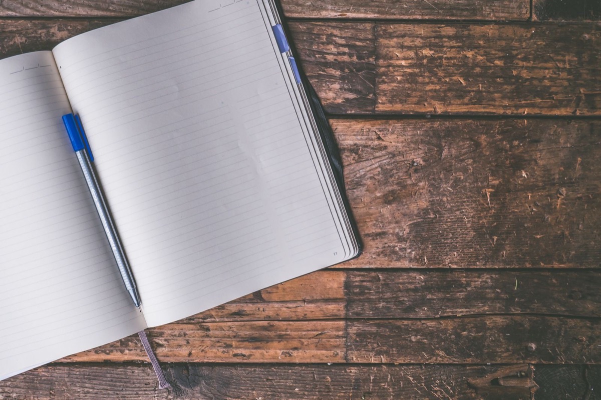 An open lined notebook with a blue pen on a dark wooden table