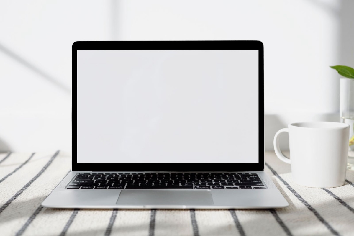 An open laptop with a blank screen on a table with a striped cloth, beside a white mug