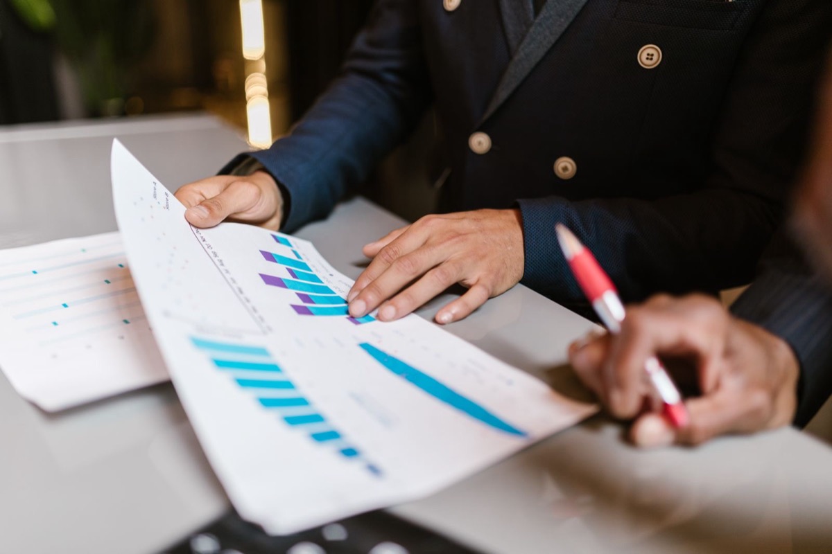 Hands pointing at printed charts with a red pen on a desk