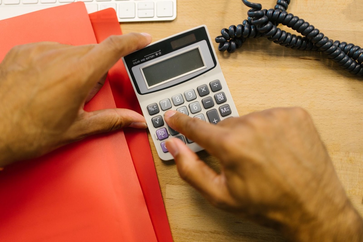 Two hands using a calculator on a red folder on a wooden desk