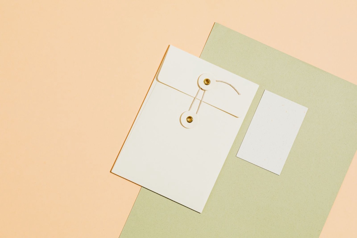 A white envelope with a string clasp and a blank card on a peach and green surface