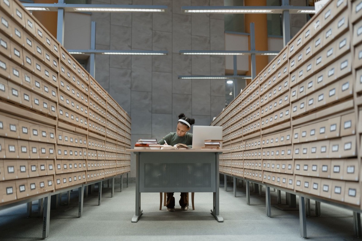 Rows of identical archive drawers in a records room, with one person at a desk in the distance