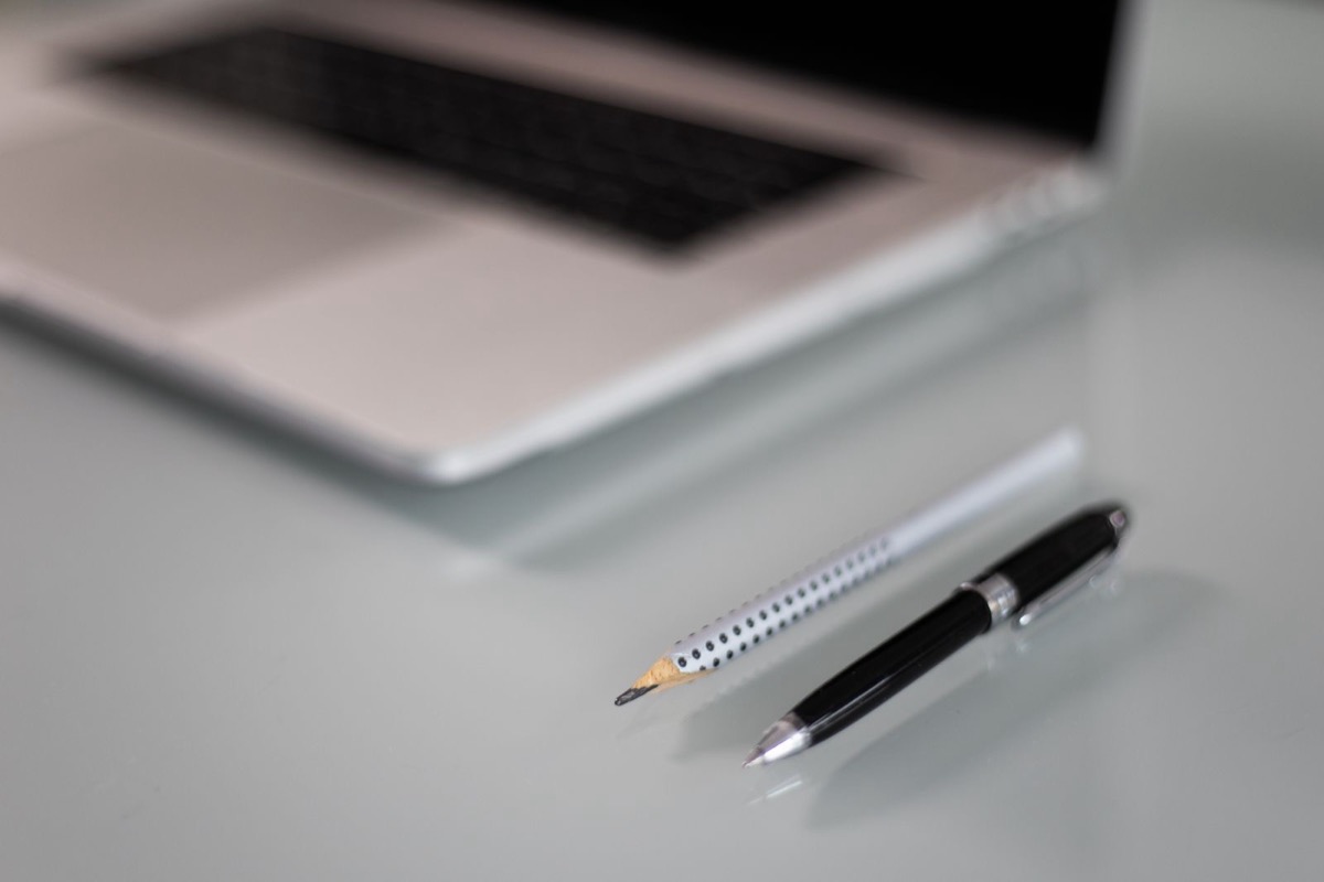 The edge of a silver laptop beside a pencil and a black pen on a white desk