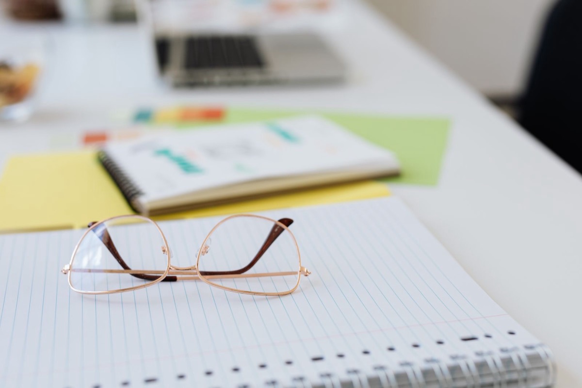 Glasses resting on a ring-bound notepad, with a notebook and coloured papers behind