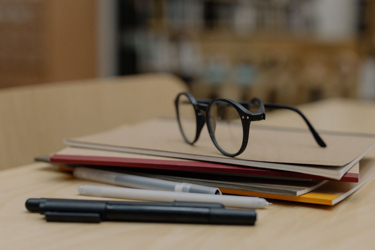 Glasses resting on a stack of notebooks with pens on a wooden table