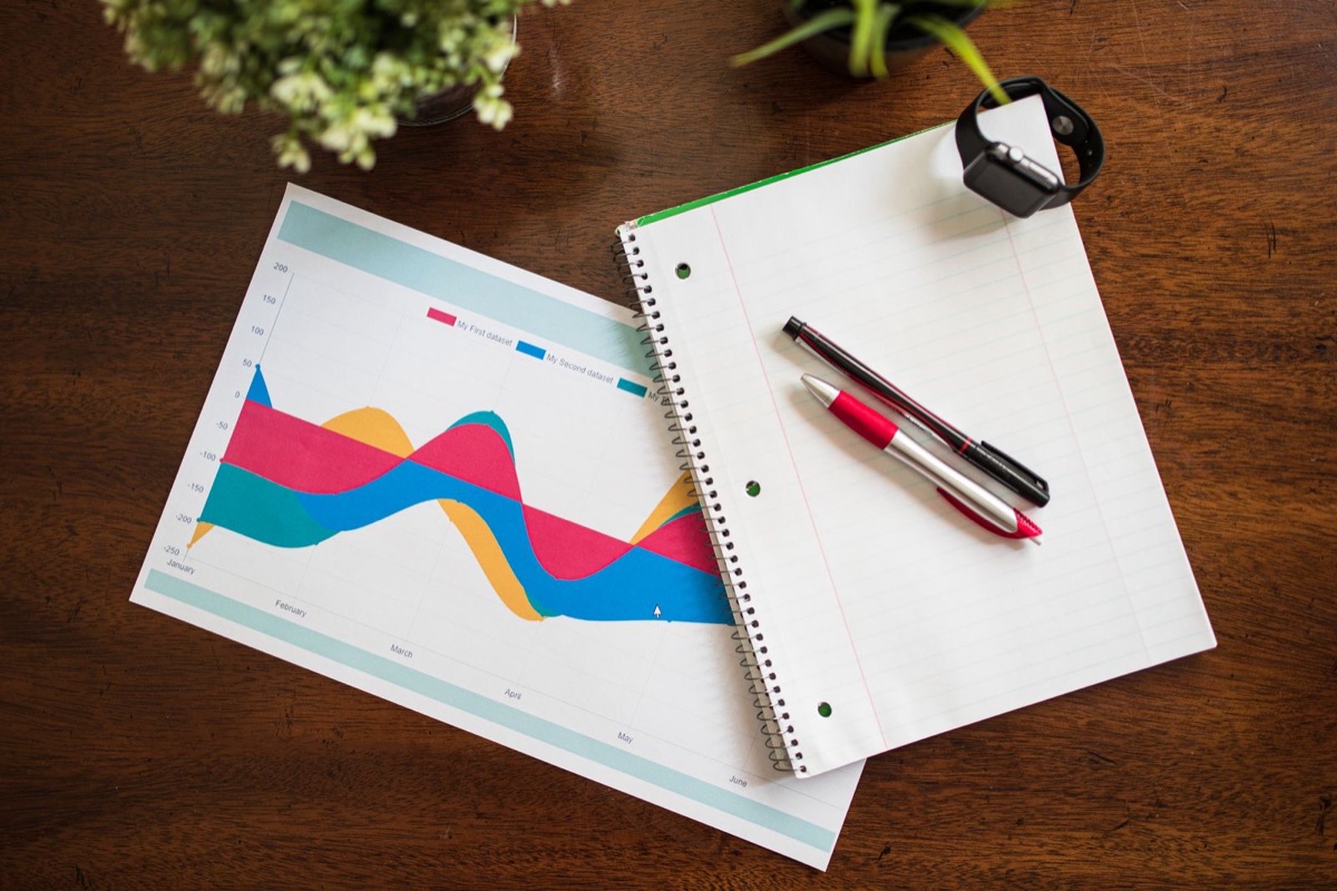 A printed colour chart, a spiral notebook, two pens and a smartwatch on a wooden desk