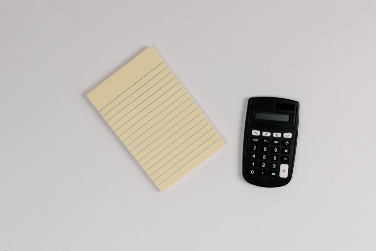 A pocket calculator beside a yellow lined notepad on a grey desk